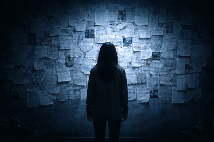 A person facing a wall covered in printed documents, representing the investigation of clairvoyant visions