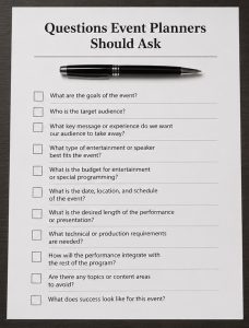 Printed checklist centered on a desk with a pen resting across it, representing questions to ask before booking a hypnosis show or mentalism show