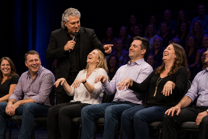 Volunteer reacting with laughter while hypnotized on stage as the audience watches